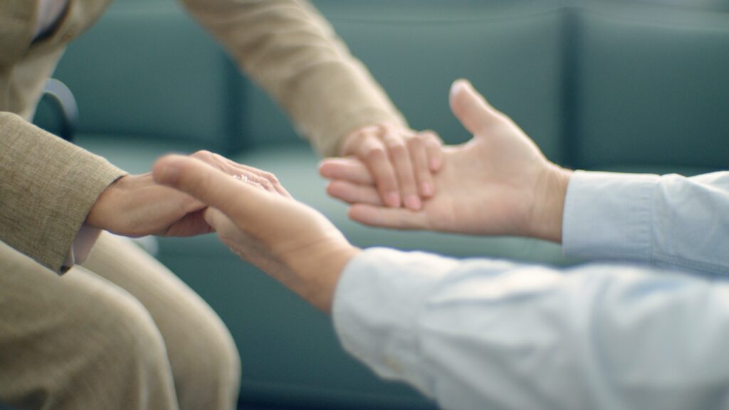 S'informer - Se former Close-up of two people holding hands, symbolizing support and compassion in a peaceful setting.